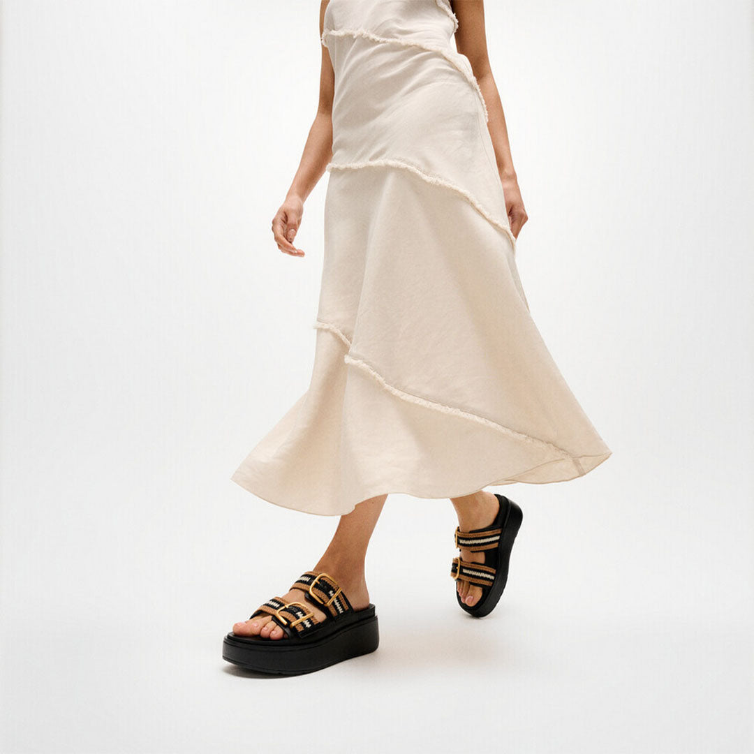 Woman wearing FitFlop GEN-FF Max Stripe-Webbing Two-Bar Slides with adjustable straps and a supportive chunky flatform sole.