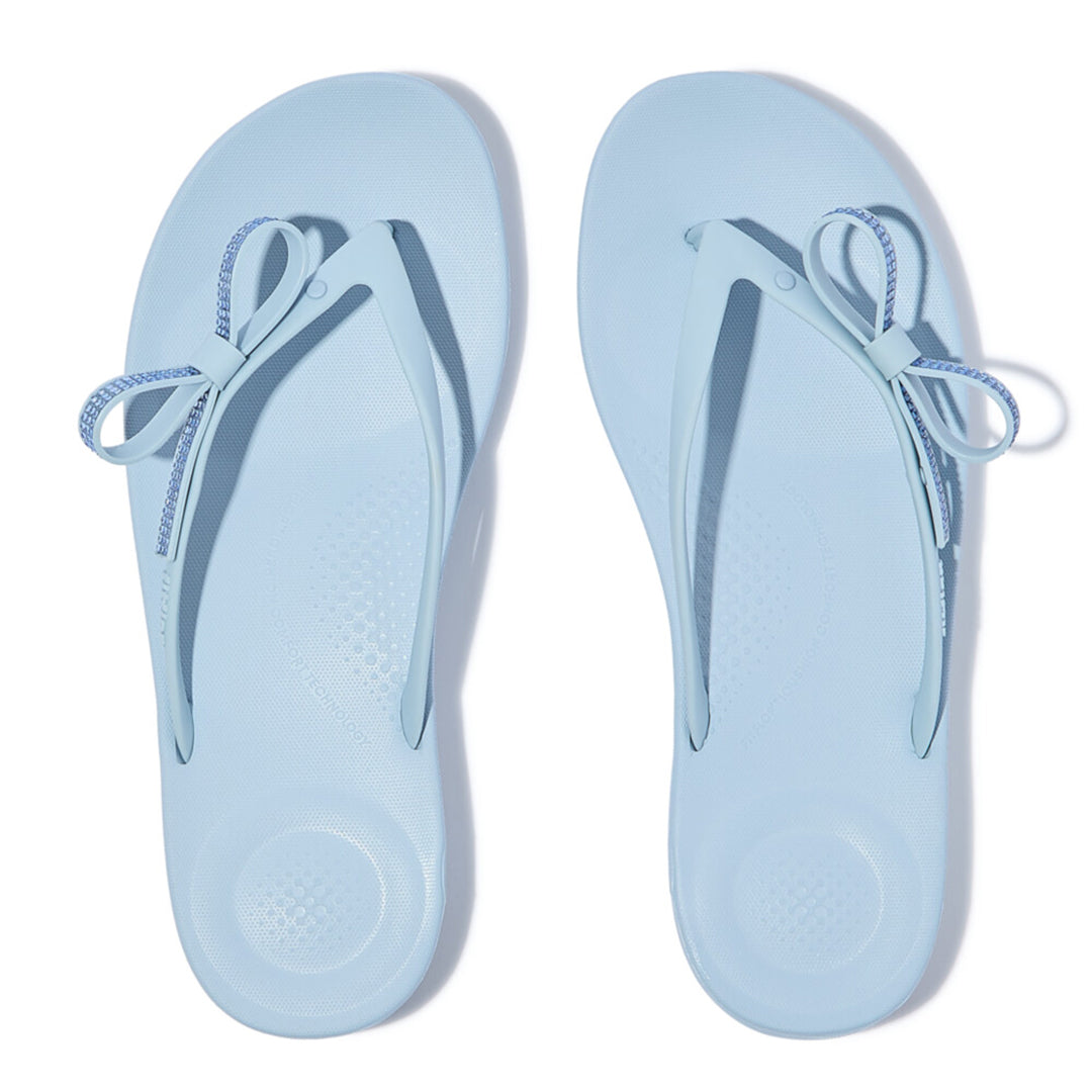 iQUSHION Glitz-Bow flip-flops with cushioned footbed, anatomically shaped straps, delicate bow detail, waterproof and lightweight.