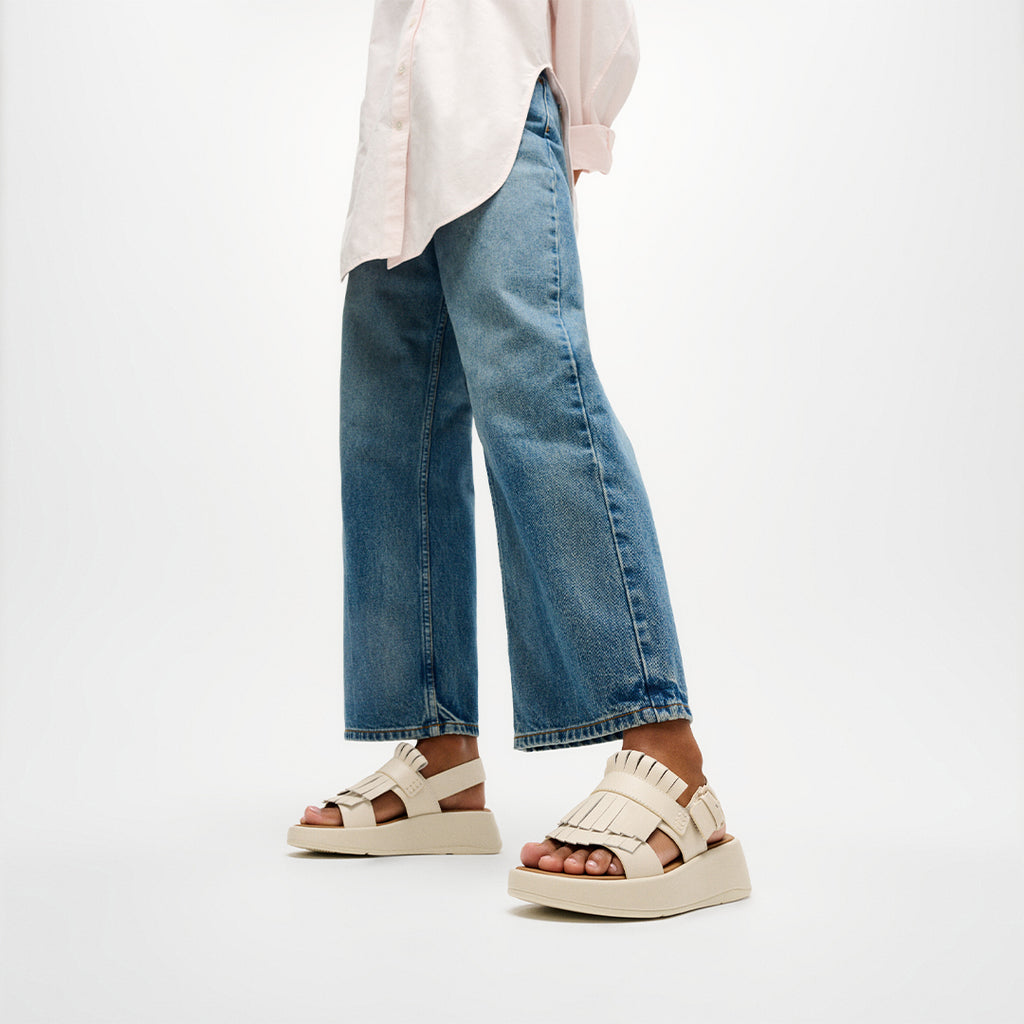Woman wearing FitFlop F-MODE Fringe Sandals with premium leather, tassel-inspired fringe, and a supportive Microwobbleboard™ sole.