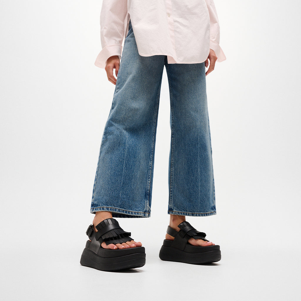 Woman wearing FitFlop F-MODE STACK Leather Fringe Sandals with premium leather construction, fringe trim, and cushioned platform sole.