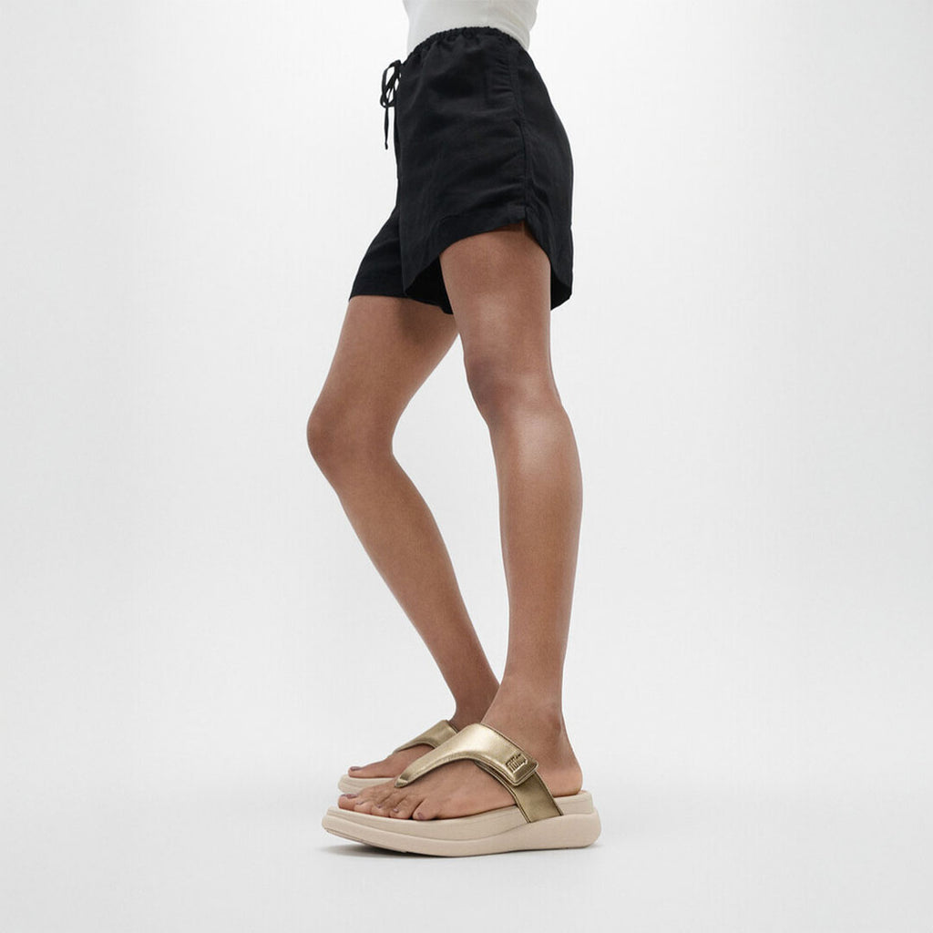 Woman wearing FitFlop F-MODE Go Toe-Post Sandals with metallic straps, ergonomic cushioning, and a lightweight flatform sole.