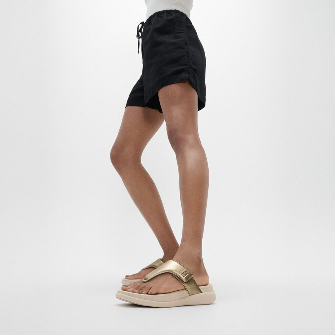 Woman wearing FitFlop F-MODE Go Toe-Post Sandals with metallic straps, ergonomic cushioning, and a lightweight flatform sole.