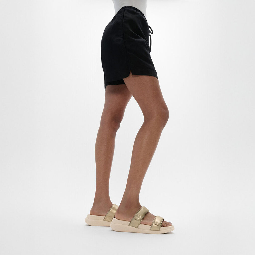 Woman wearing FitFlop F-MODE Go Two-Bar Slides with metallic straps, cushioned footbed, and lightweight flatform sole.