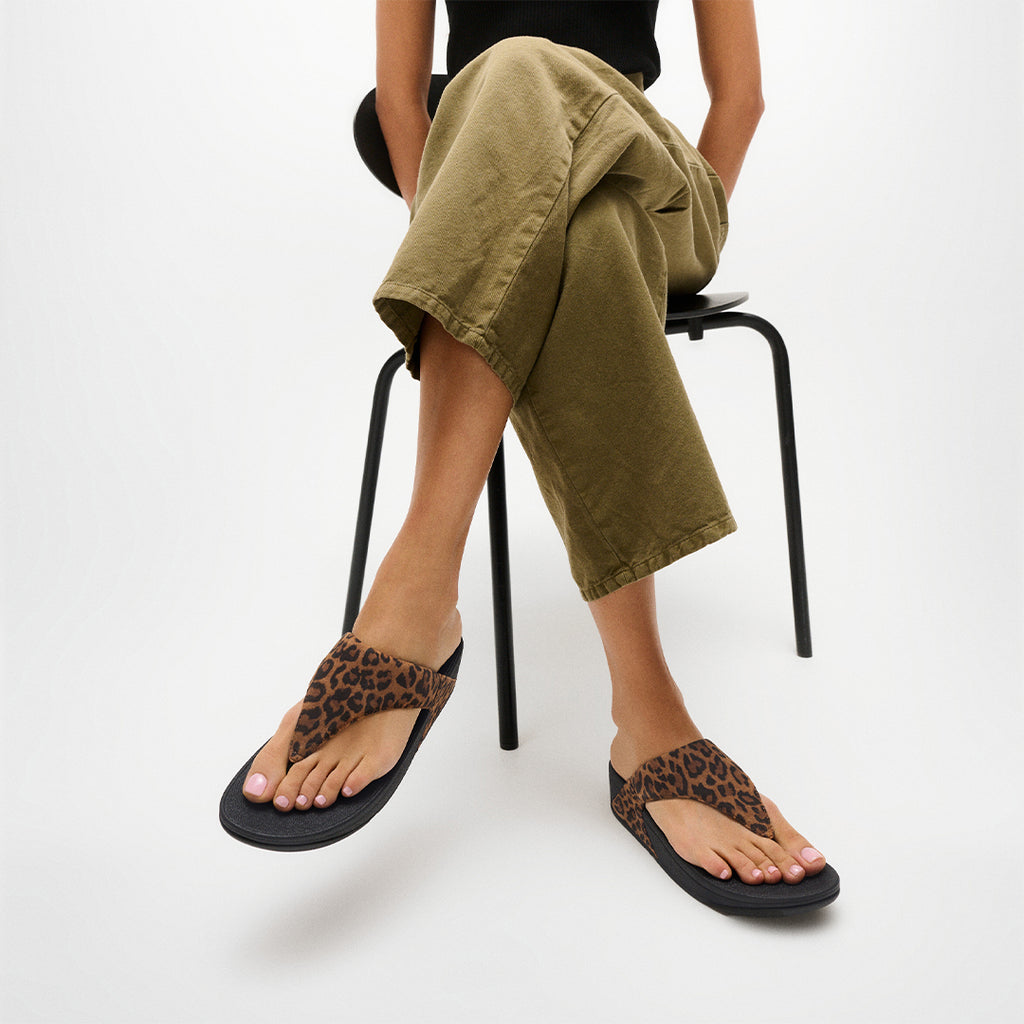 Woman wearing FitFlop LULU Suede Leopard Toe-Post Sandals with soft suede straps and supportive cushioned sole.