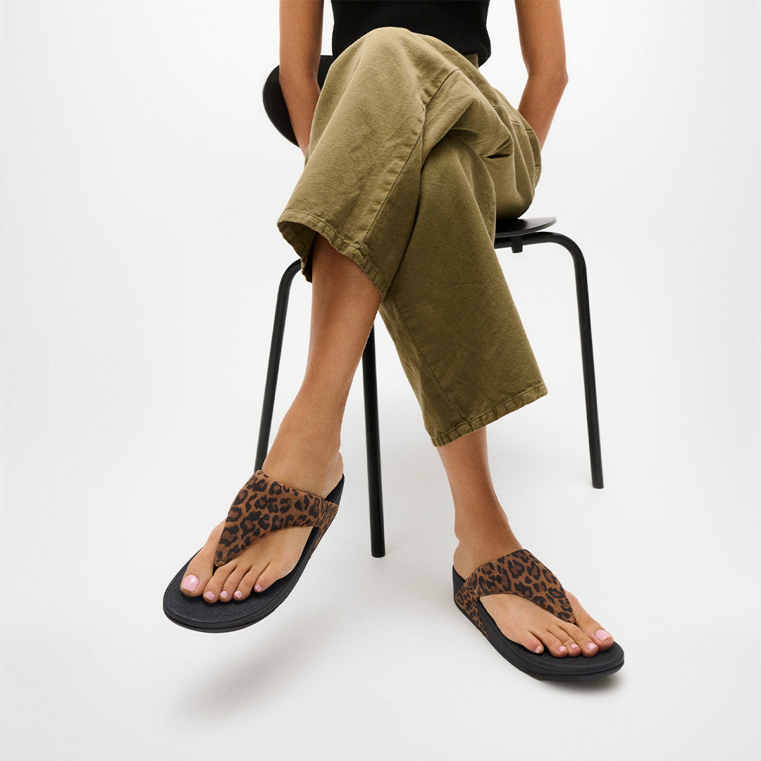 Woman wearing FitFlop LULU Suede Leopard Toe-Post Sandals with soft suede straps and supportive cushioned sole.