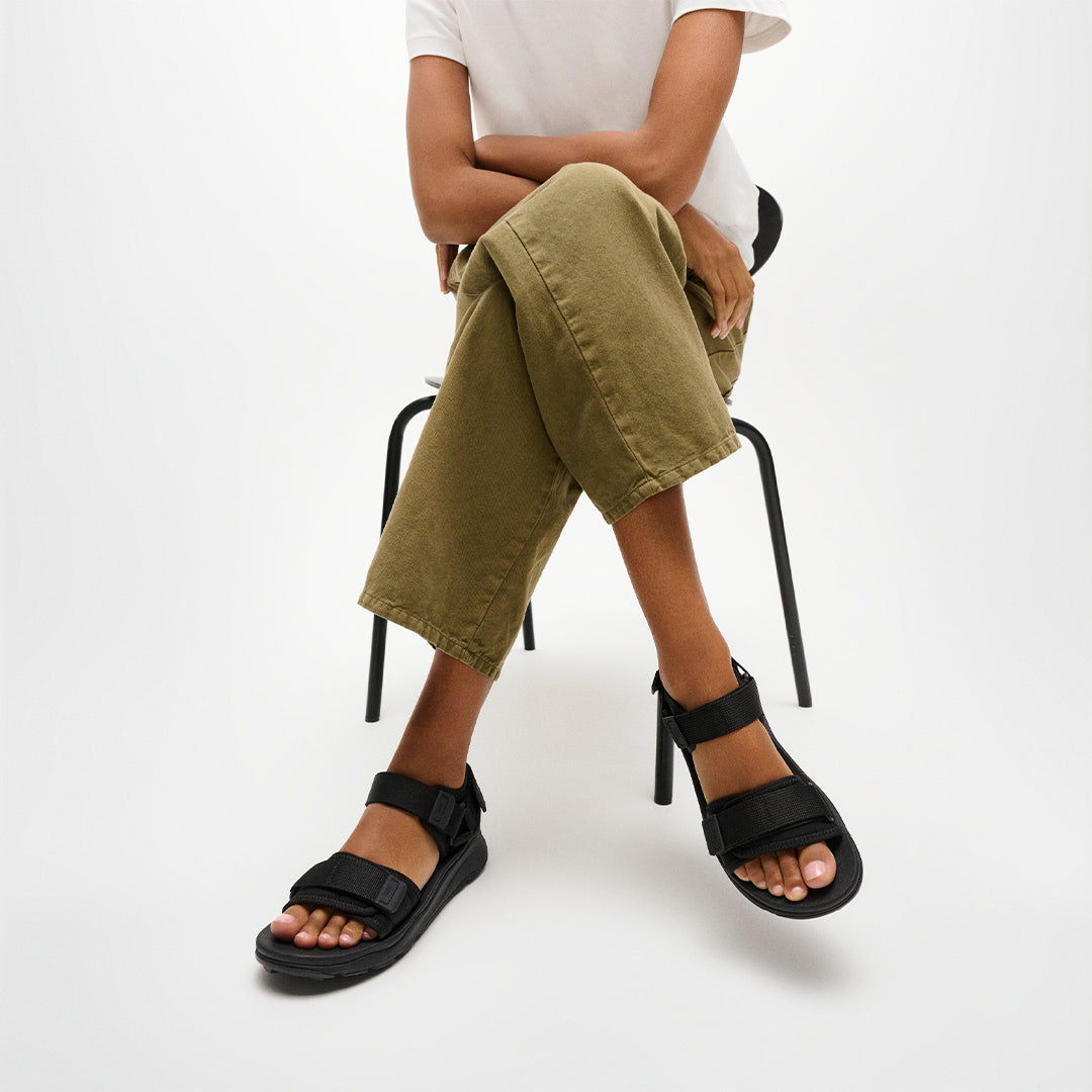 Person wearing FitFlop NEO-D-HYKER Outdoor Sandals featuring adjustable straps, ergonomic cushioning, and durable outdoor traction.